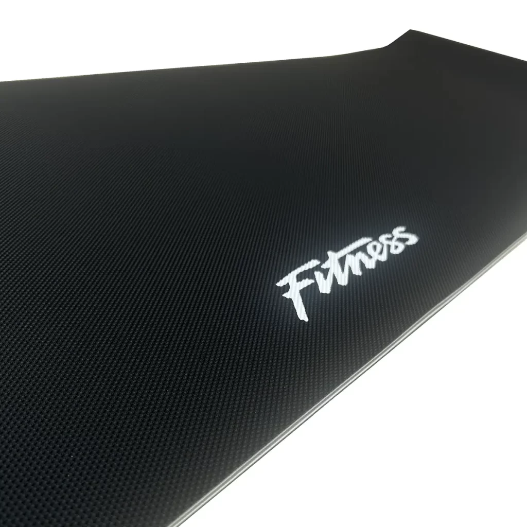 A close-up view of a black exercise mat with a textured surface and the word Fitness printed in white on one corner.