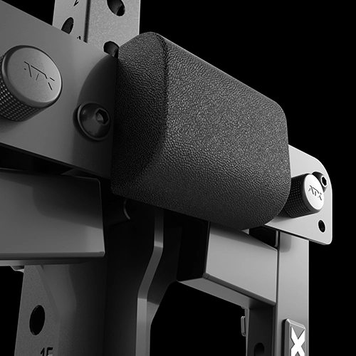 Close-up of a black padded support attached to a sturdy metal gym machine, featuring textured adjustment knobs and bolts, with the ATX logo visible on several parts, set against a black background.