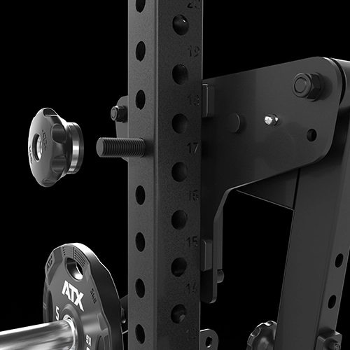 Close-up of a black gym rack with numbered holes, adjustment knobs, and a weight plate marked “ATX 5 KG” on a barbell. The background is plain black.