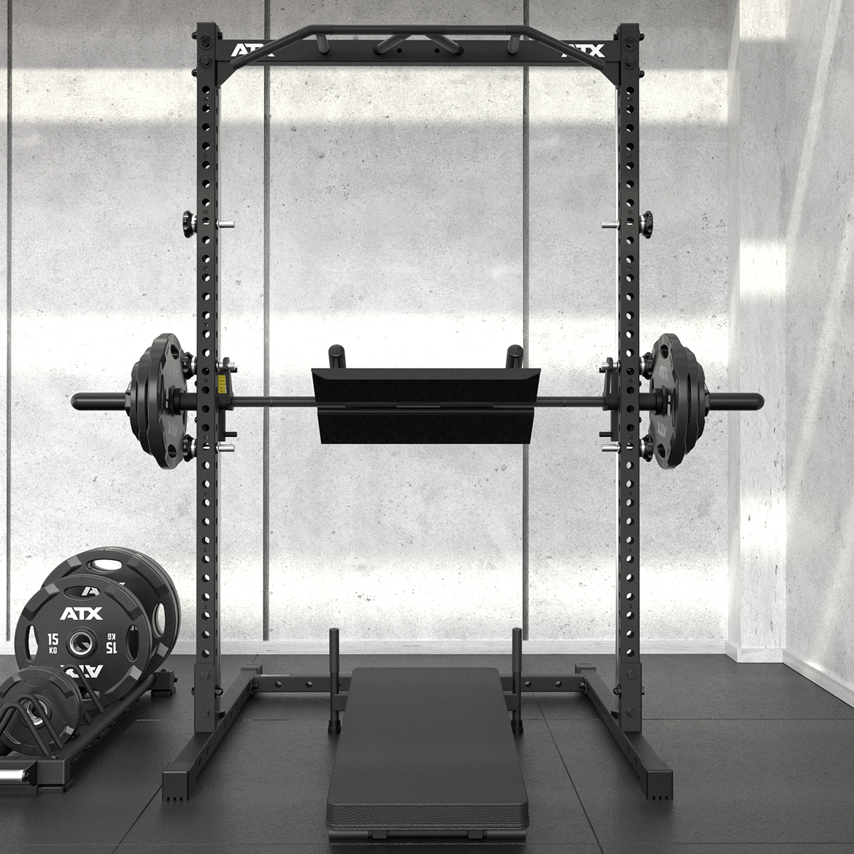 A power rack with a loaded barbell and a black safety attachment in a minimalist gym setting. Weight plates are stacked on the floor to the left, and a flat bench is positioned inside the rack.