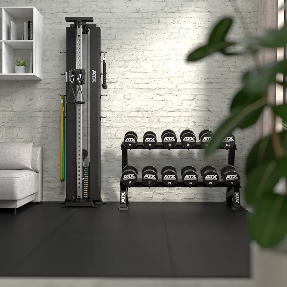 A modern home gym features the ATX® Single Cable Station - Wall Mounted, a rack of black medicine balls with visible weights, a white couch, white shelves on a light brick wall, and a green plant bringing freshness to the space.