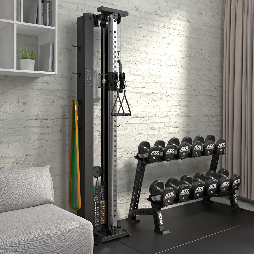 A home gym setup featuring the ATX® Single Cable Station - Wall Mounted, resistance bands, a rack of black ATX dumbbells, a gray sofa, and shelves on a light brick wall.