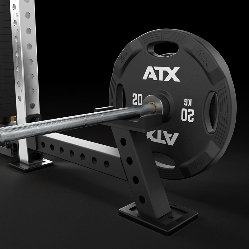 A close-up view of a barbell loaded with a 20 kg ATX weight plate, resting on a black metal squat rack against a dark background.