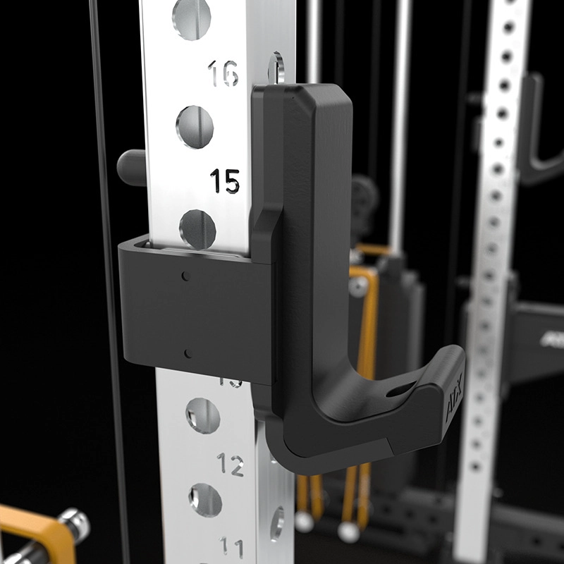 Close-up of a black J-hook attached to a silver metal squat rack with numbered holes, used for holding a barbell in a gym setting. The background shows gym equipment and weight cables.