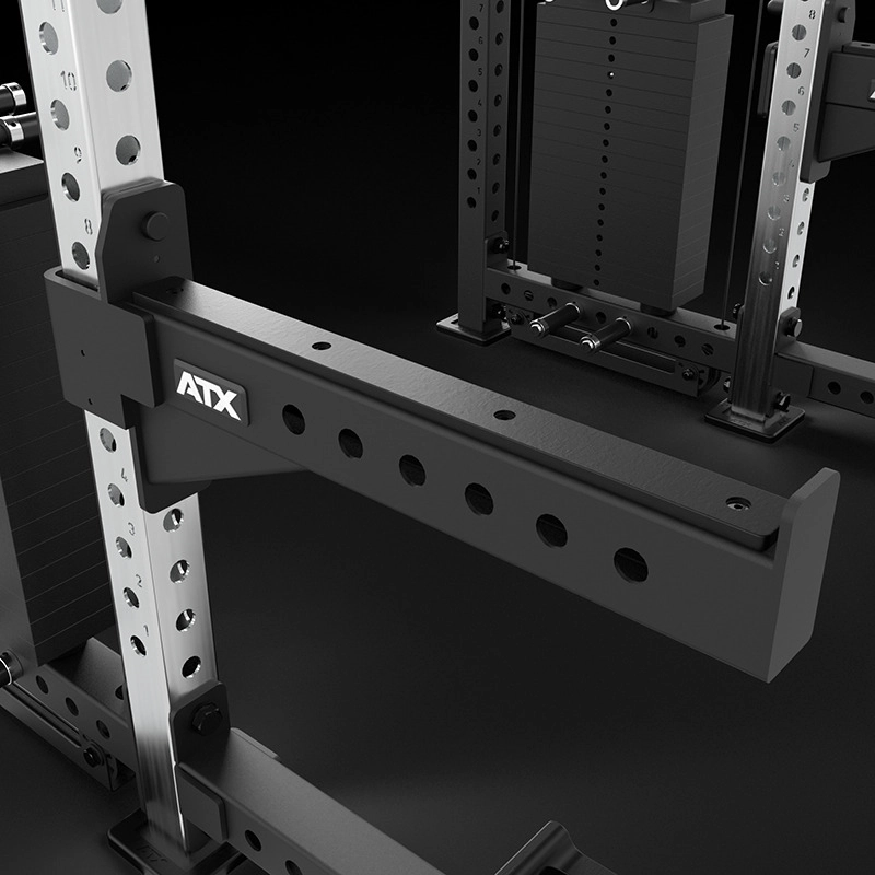 Close-up of a black and silver ATX gym power rack with a labeled horizontal safety arm and weight stack in the background, used for strength training and weightlifting exercises.