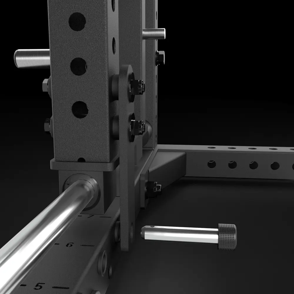 Close-up view of a black metal power rack with multiple holes, adjustment pins, and a steel barbell loaded on a support arm. The background is dark, highlighting the gym equipment’s sturdy construction.