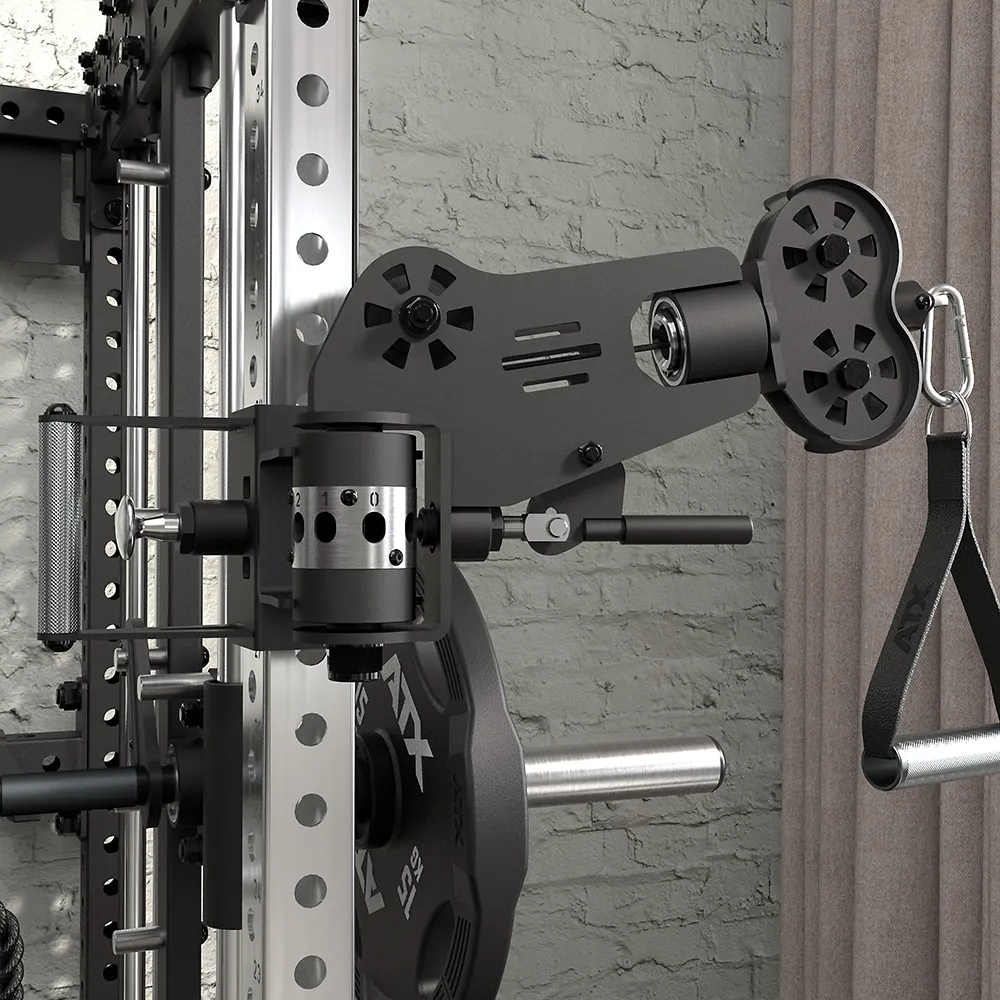 Close-up of a cable gym machine attachment mounted on a metal squat rack, with adjustable pulleys, weight plates, and a strap handle, against a brick wall and curtain.