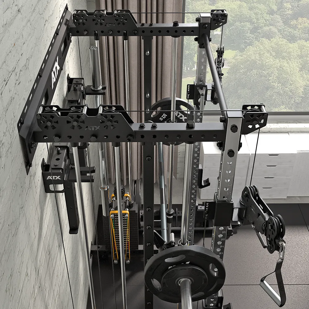 A compact home gym setup features the ATX® Squat Rack with Cables (Copy), complete with weight plates, pulleys, and attachments, all arranged near a large window overlooking scenic trees.