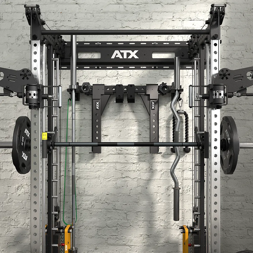 A close-up of the ATX® Squat Rack with Cables (Copy) stands before a textured gray brick wall, shown with weight plates, resistance bands, and both standard and EZ curl barbells.