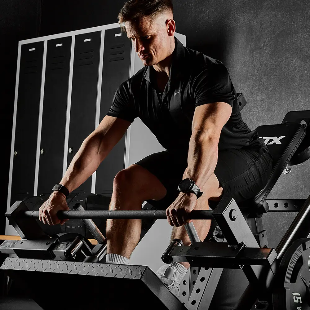 A man dressed in black gym clothes performs a rowing exercise with a barbell on the ATX® Smith Row Machine in a gym setting, with lockers visible in the background.