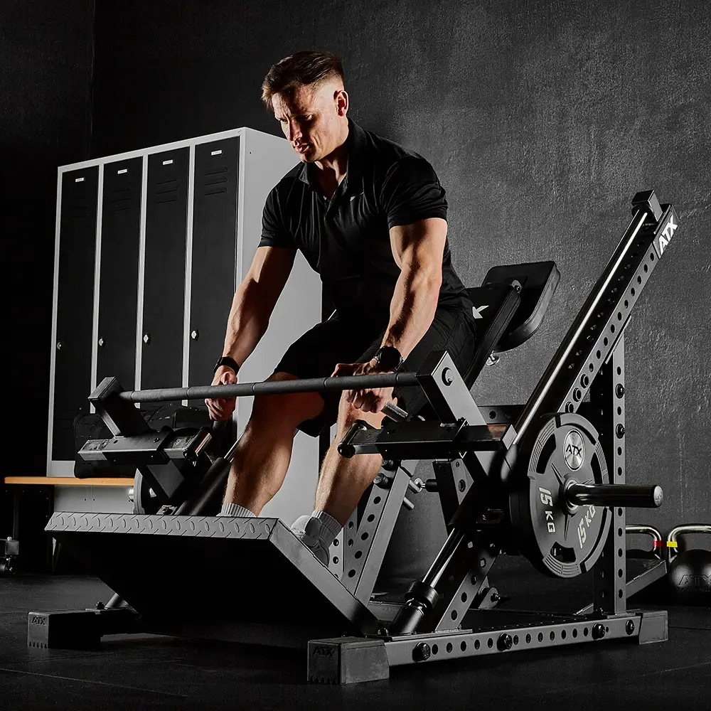 A man in a gym is using the ATX® Smith Row Machine with weights, gripping the handles and visibly straining from exertion during his workout. Lockers and a bench can be seen in the background.