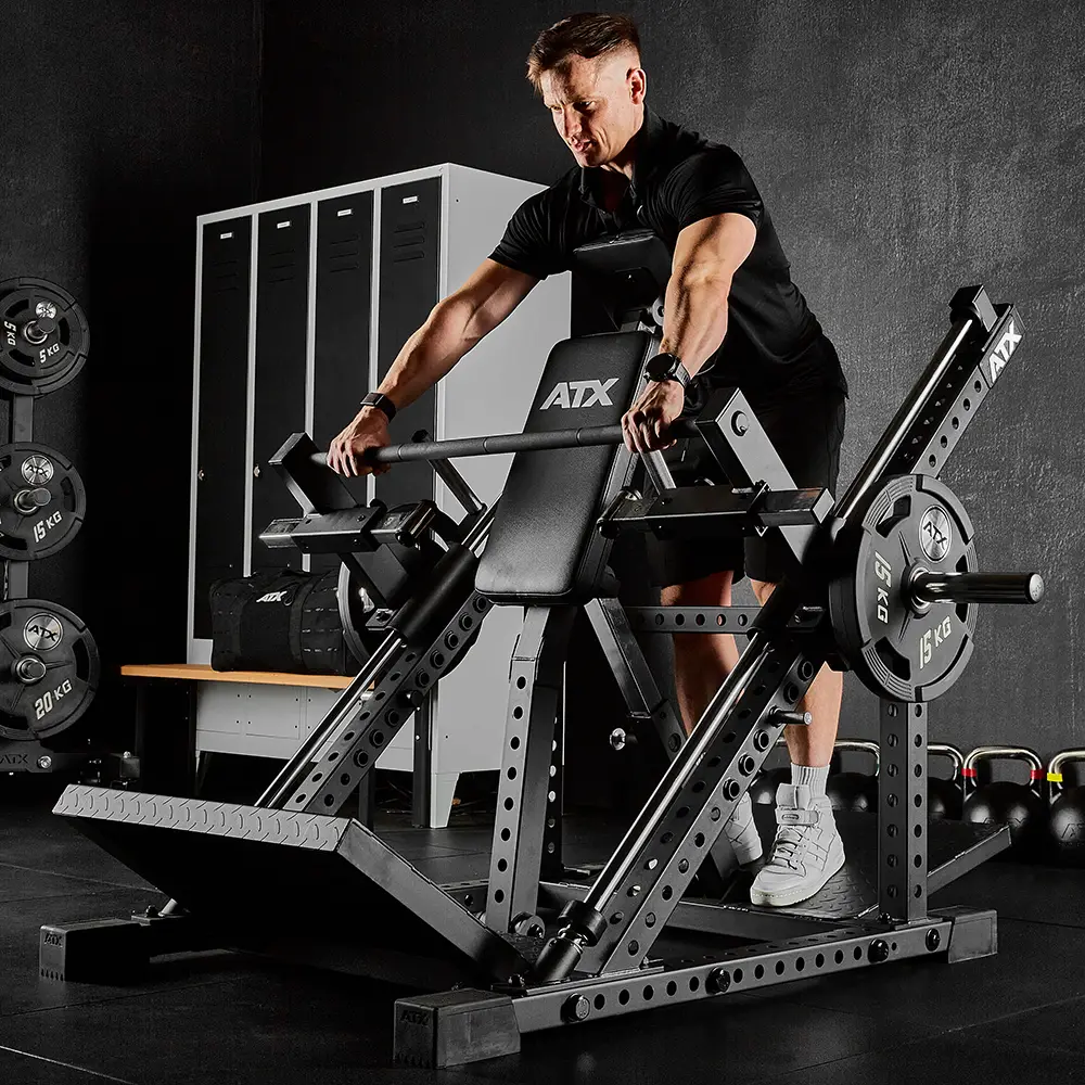 A person in athletic wear uses an ATX® Smith Row Machine with weight plates in a gym, with lockers, benches, and additional weights visible in the background.