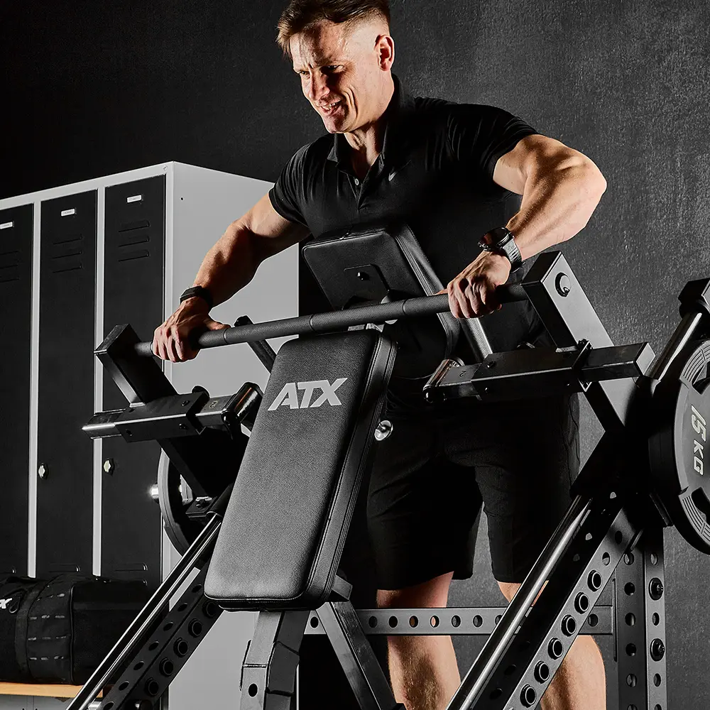 A man in a black shirt and shorts works out intensely on an ATX® Smith Row Machine, lifting weights in a gym with lockers in the background.