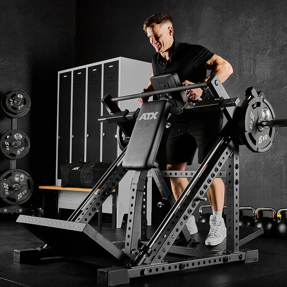 A person uses an ATX squat machine in a gym, lifting weights. There are kettlebells, dumbbells, an ATX® Smith Row Machine, and lockers in the background.