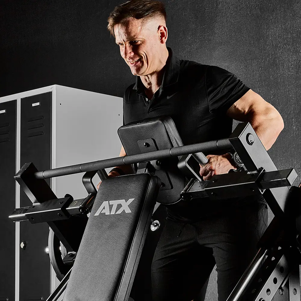 A man in a black shirt uses an ATX® Smith Row Machine for a strength training exercise in a fitness room with lockers in the background.