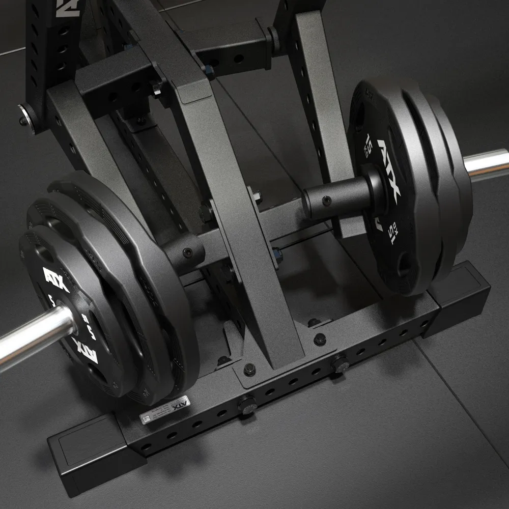 Close-up view of a black metal weightlifting machine with adjustable holes and a barbell loaded with large weight plates, positioned on a dark gym floor.