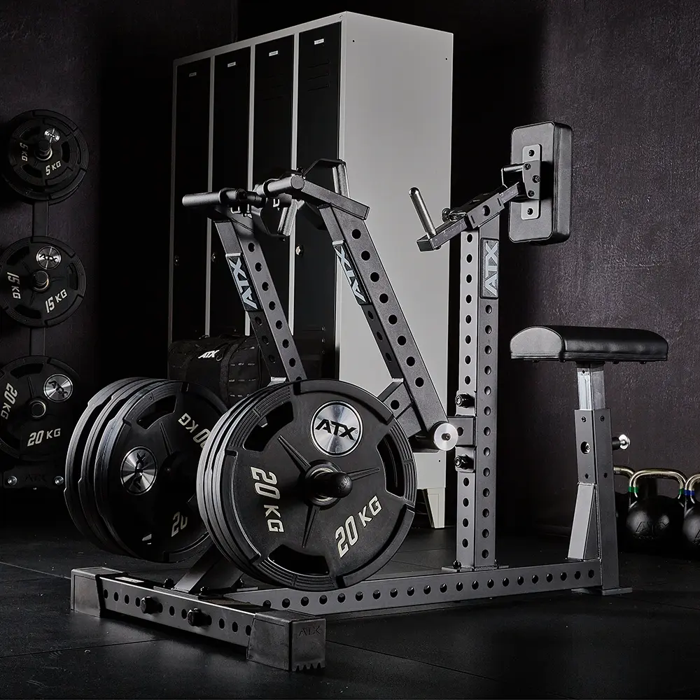 An ATX® Chest Supported Row Machine loaded with several 20 kg weight plates, with black lockers in the background and barbells plus kettlebells nearby, all set on a dark gym floor.