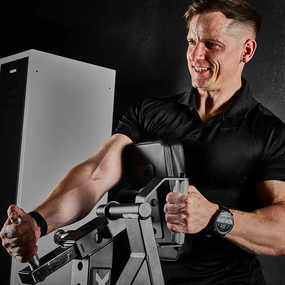 A man in a black shirt smiles while using a bicep curl machine in a gym, gripping the handles with both hands as he works out near the ATX® Chest Supported Row Machine.