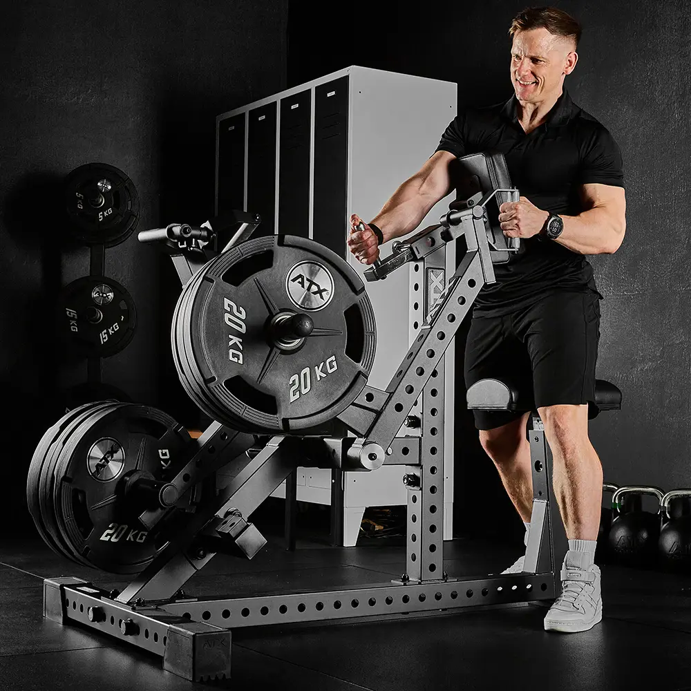 A man dressed in black works out on the ATX® Chest Supported Row Machine for an upper body exercise in a dimly lit gym, with weights, lockers, and kettlebells visible in the background.