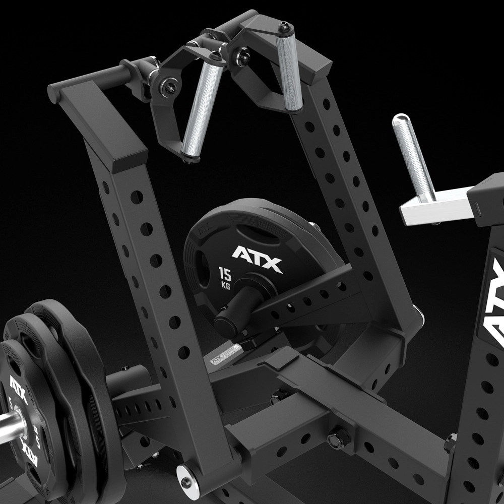 Close-up of a black ATX gym machine with adjustable arms and 15 kg weight plates attached. The equipment has a sturdy, industrial design with multiple holes for customization.
