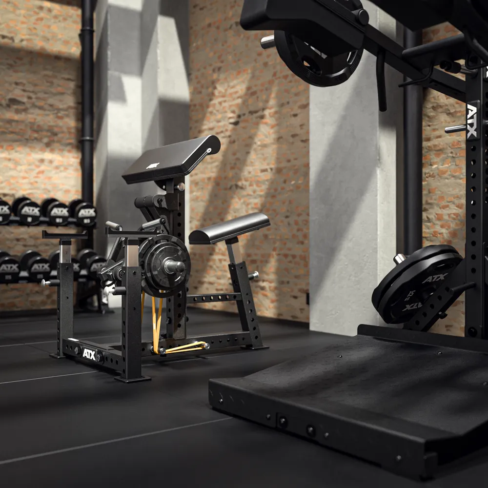 A modern gym with the ATX® Bicep Blaster Preacher Curl Machine, benches, a squat rack, weight plates, and dumbbells, all set against brick walls and a black rubber floor.