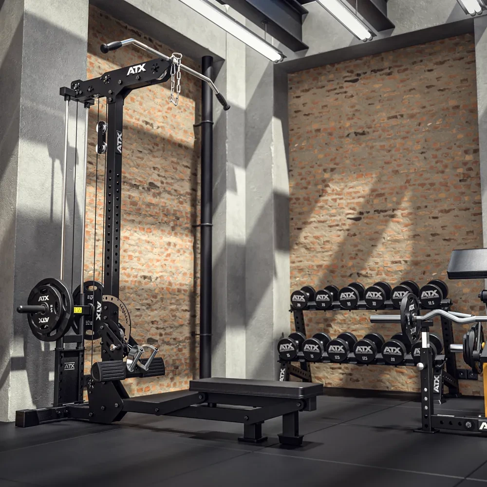 A modern gym with a cable machine, weight plates, and a rack of dumbbells, all branded ATX, is set against a brick wall with large windows letting in natural light.