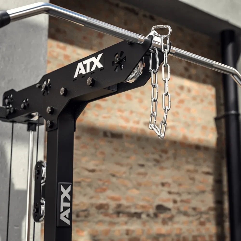 Close-up of an ATX-branded gym machine with a metal chain hanging from a horizontal pull-up bar, set against a brick wall and concrete pillar in a fitness facility.