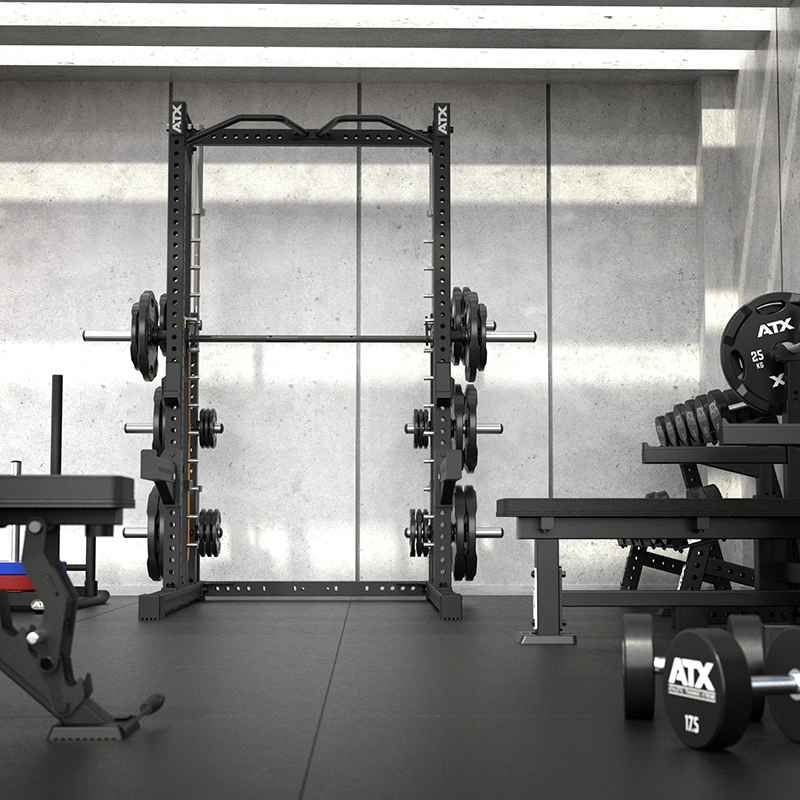 Modern gym featuring the ATX Commercial Smith Machine, along with a squat rack, weight plates, benches, dumbbells, and barbells on a black floor with concrete walls and natural light streaming in from above.