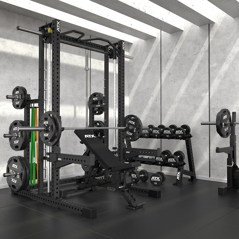 Modern gym with a squat rack, adjustable bench, barbell plates, ATX Commercial Smith Machine, and weighted bars in a bright, concrete room with angled ceiling lights.