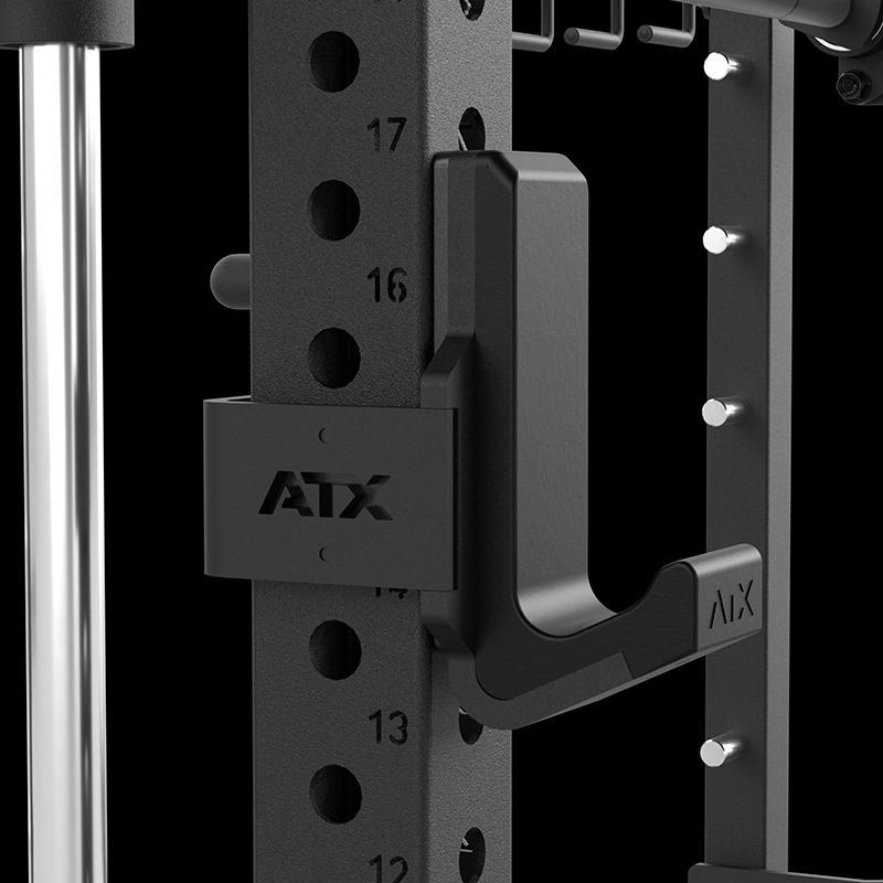 Close-up of a black ATX gym rack with numbered holes, a sturdy metal hook, and barbell holder attachment against a dark background.