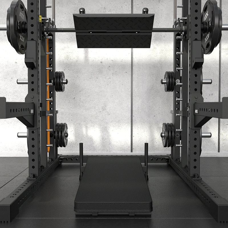 A close-up of a black gym squat rack and the ATX Commercial Smith Machine, equipped with weight plates, safety bars, and a bench positioned in the center, set against a gray concrete wall.