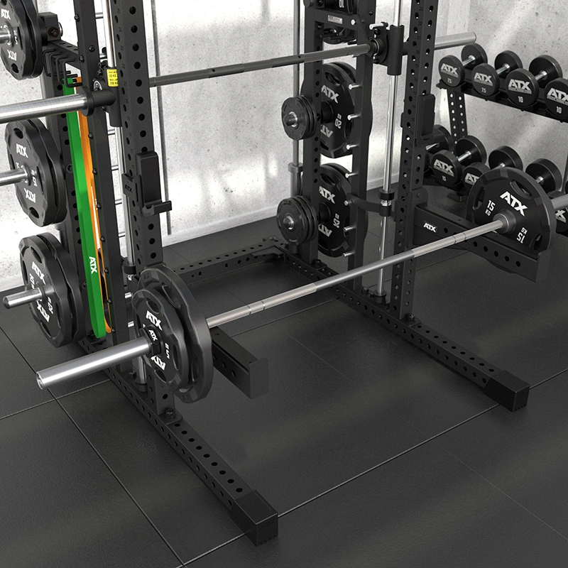 A gym squat rack with a loaded barbell, weight plates, resistance bands, and dumbbells on racks sits on black tiled flooring against a concrete wall—creating a professional setup perfect for complementing the ATX Commercial Smith Machine in your fitness space.