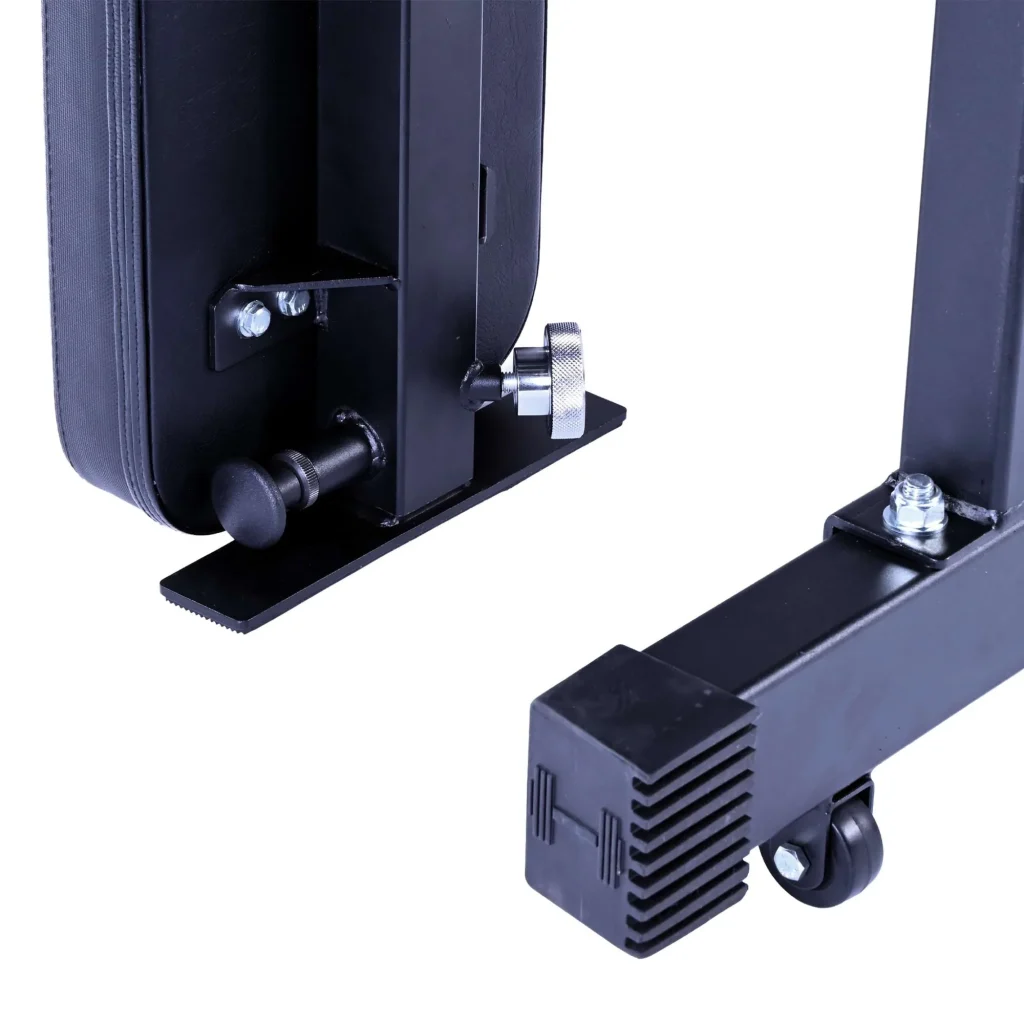Close-up of black metal parts on the Kickstand for Super Bench, featuring bolts, a knurled knob, a padded section, and wheels on the base for mobility.