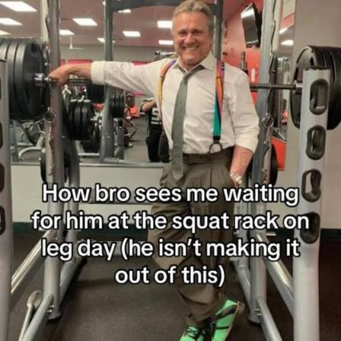 Smiling older man in dress clothes, colorful suspenders, and green shoes stands confidently by a loaded squat rack at the gym. Text reads: How bro sees me waiting for him at the squat rack on leg day (he isn’t making it out of this). The perfect inspiration for your next home gym guide.
