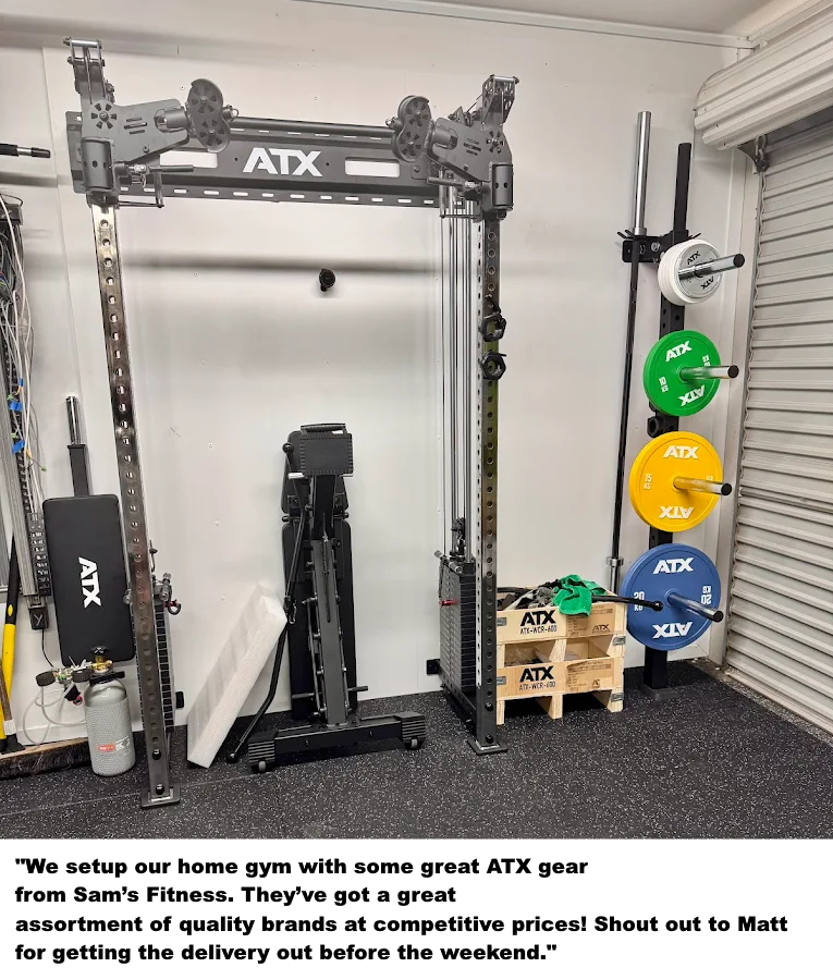 A home gym guide setup with an ATX cable machine, weight plates on a rack, a bench, gym accessories, and a pallet of ATX boxes in a garage with a metal roller door.